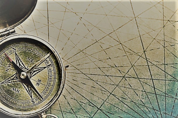 A close up of a compass as it rests on the converging navigational lines of an old map.